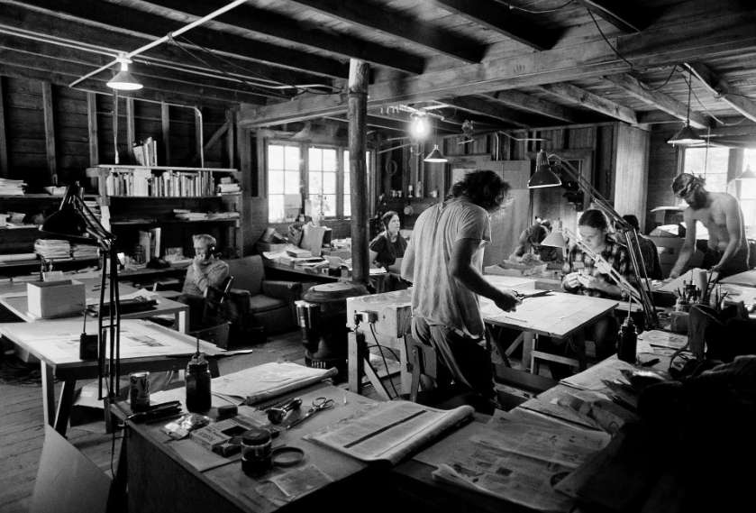 Five people in a work room sitting and standing at work stations 